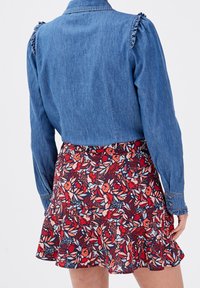 Denim shirt met gerimpelde schouderaccenten, gecombineerd met een wijde bloemenrok met rode, blauwe en witte patronen.