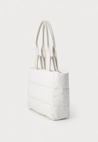 Sac fourre-tout matelassé blanc avec double poignée sur le dessus, présentant une surface texturée et une fermeture zippée. Accent doux sur les bords des poignées.