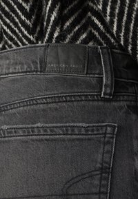 Schwarze Denim-Jeans mit feiner Textur, ausgestattet mit einem geprägten Lederpatch und einem mittelhohen Bund, sowie klassischen Gesäßtaschen.