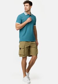 Blå polo skjorte med hvid detaljer, parret med beige cargo shorts med flere lommer. Modellen har hvide sneakers på.