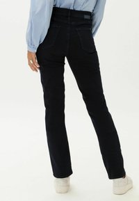 Schmal geschnittene, dunkelblaue Jeans aus Denim mit Taschen, mittelhoher Taille und subtilen Stickdetails, kombiniert mit weißen Sneakern.