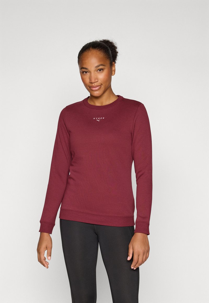 Burgunderfarget genser med rund hals og ribbede mansjetter. Har en liten hvit logo på brystet. Kombinert med svarte leggings.