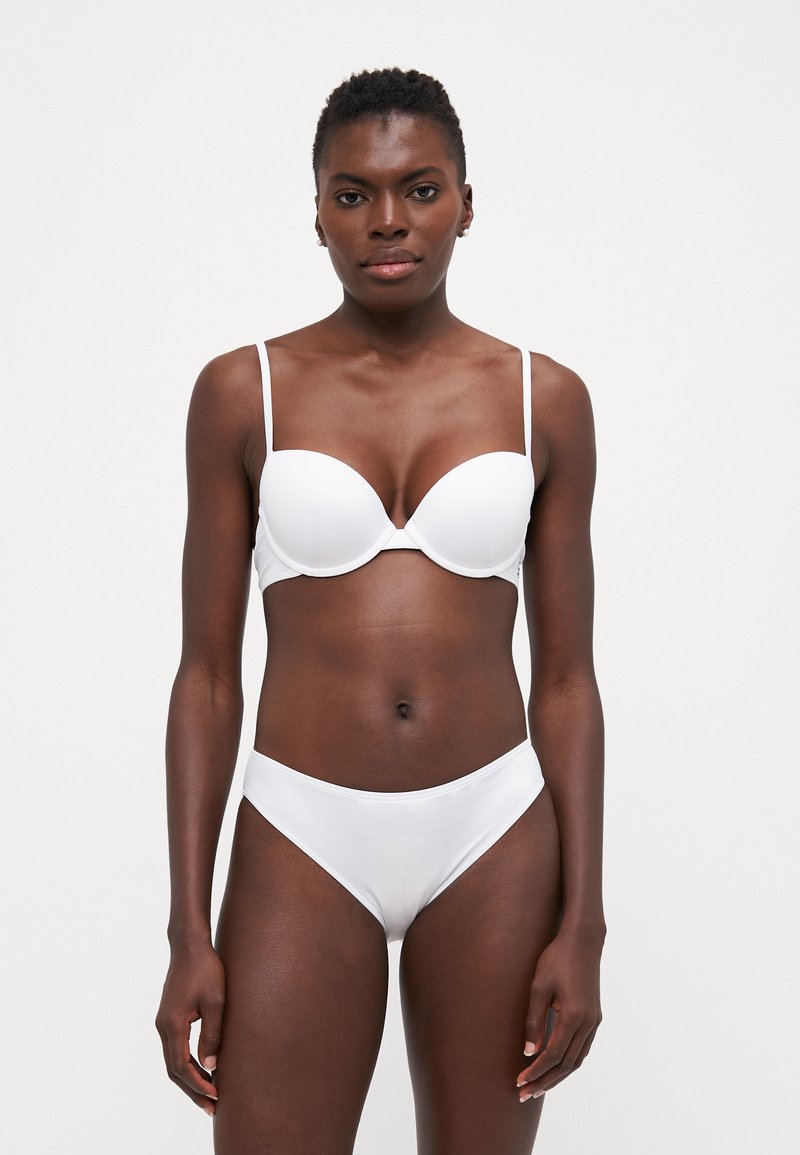 Reggiseno bianco con coppe imbottite e spalline sottili regolabili, abbinato a slip hipster bianchi. Tessuto liscio e elasticizzato con dettagli minimi.