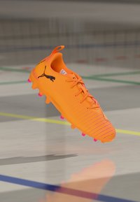 Bright orange soccer cleat with textured upper, pink accents on the sole, and a black logo. Features a traditional lace-up design.