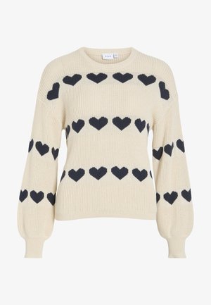 Kreemjas kootud kampsun mustade südamekujude mustriga rinnal, varrukatel ja õlgadel, pikkade läikivate varrukatega ning ümara kaelusega.