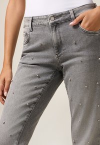Jeans de mezclilla gris con un diseño ajustado, que cuenta con adornos redondos dispersos. Incluye un cierre de botón y un bolsillo lateral.