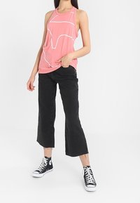 Canotta senza maniche rosa chiaro con disegno geometrico bianco, abbinata a jeans cropped neri a vita alta e sneakers nere alte.