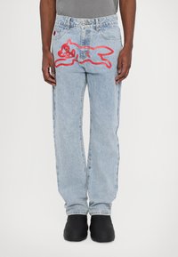 Jeans din denim de un albastru deschis cu un croi relaxed, având un mare design brodat cu un pisoi de desene animate roșu pe spate și o ușoară decolorare.
