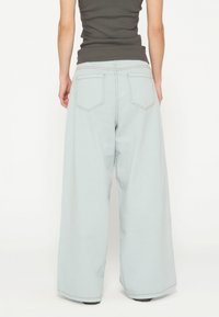 Jeans a gamba larga di colore blu chiaro con vita alta, tasche posteriori e dettagli di cucitura discreti. Materiale morbido e traspirante con una texture liscia.