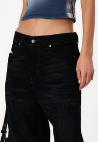 Svarte dongeri jeans med rett snitt, med subtile mønster variasjoner, sølvfarget hardware og kontraststingingsdetaljer.