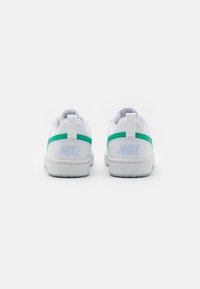 White sneakers with a smooth texture, green accents on the heel, and a visible logo in light blue. Rounded toe and low-top design.