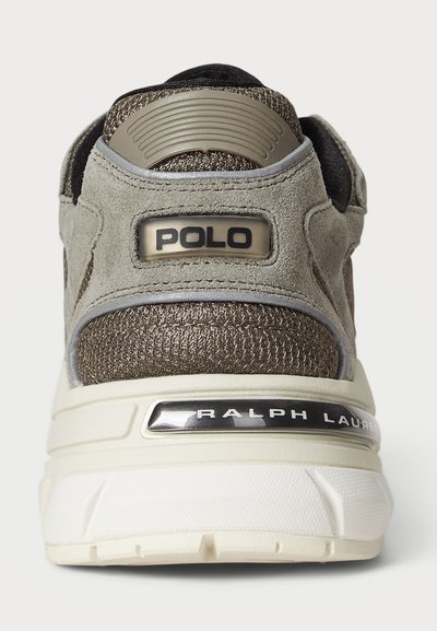 Pelēki zamšādas sneakeri ar metāliskām akcentiem, paaugstinātu papēdi un teksturētu audumu; aizmugurē ir "POLO" un "RALPH LAUREN" zīmols.
