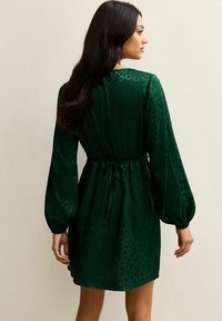 Vestido verde con estampado de leopardo, cinturado en la cintura, con mangas largas abullonadas y textura suave. Detalle elástico en la parte trasera.