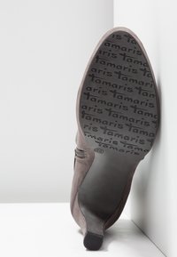 Semelle de botte à talon pour femme avec motif antidérapant "tamaris", tige en suède, fermeture éclair latérale et marquages de taille 39, inclinée contre des surfaces blanches.