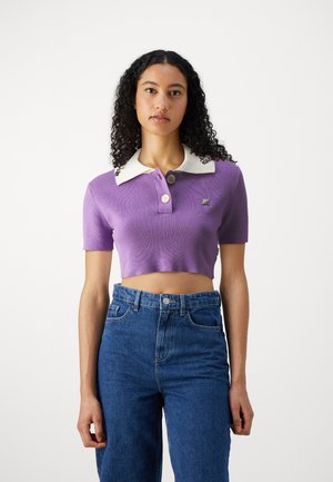Purple cropped polo shirt with a white collar, featuring two buttons. Worn with high-waisted blue denim jeans. Smooth texture.