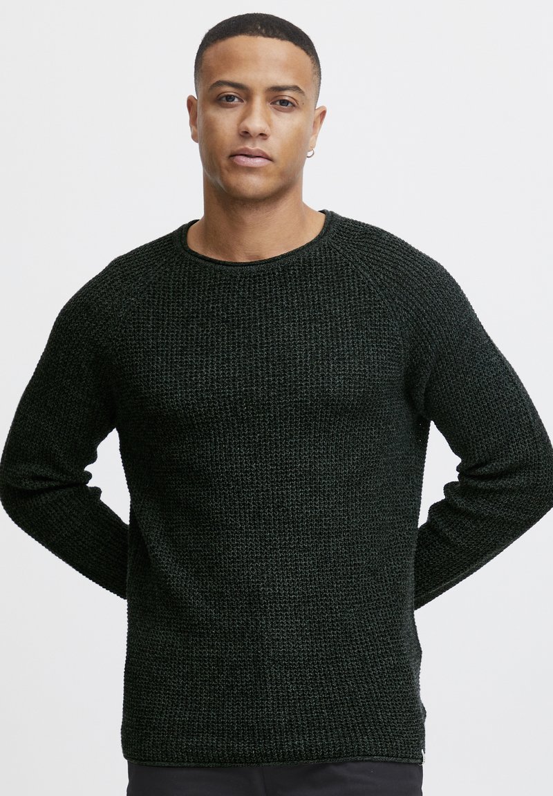 Dark green knitted sweater with a textured pattern, round neckline, and long sleeves, featuring ribbed cuffs and hem.