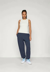 Ljusgrå ärmlös topp i kombination med lösa marinblå joggingbyxor, bärs med vita sneakers. Slätt tyg; enkel, strömlinjeformad design.