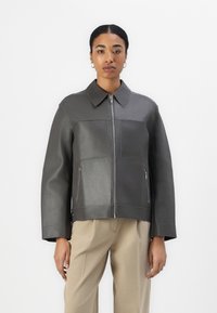 Graue Lederjacke mit durchgehendem Reißverschluss, großem Kragen und zwei seitlichen Reißverschlusstaschen. Verfügt über eine kastige Form und gestickte Details überall.