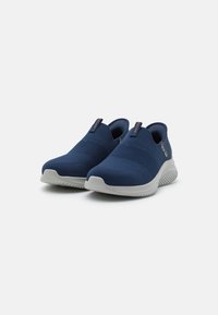 Marineblå strikkede slip-on sko med teksturert overdel, kontrasterende lys grå gummisåle og minimalt design. Har en liten logo detalj.