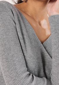 Harmaa ribbineuloksinen paita V-kaula-aukkolla. Pehmeä pinta, jossa hienovarainen kiilto. Pitkät hihat, joissa vartalonmyötäiset hihansuut. Lähikuva kankaasta.