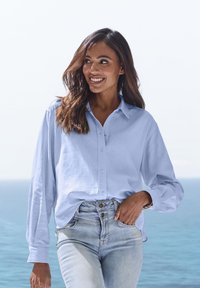 Light blue button-up shirt with long sleeves, relaxed fit, and collar; paired with high-rise light denim jeans. Casual, textured fabric.
