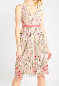 Blommönstrad klänning i mjuk rosaton med V-ringning. Har en figursydd midja, ett subtilt rosa bälte och en flytande kjol som når knäna.