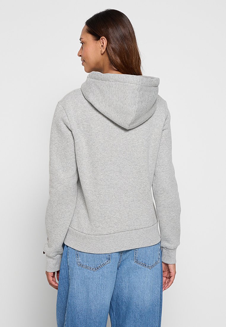 Felpa grigia realizzata in morbido tessuto, con cappuccio regolabile, polsini a costine e vita aderente. La vista posteriore mostra un design minimalista senza loghi.