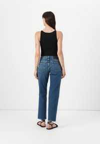 Top en maille côtelée noire, jeans en denim bleu taille haute, design à jambes droites, deux poches arrière, porté avec des sandales à lanières noires.