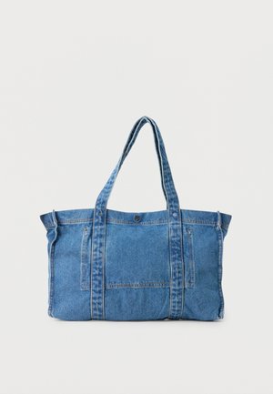 Blå denimnettaske med to lange håndtag og en forlommer, sat op mod en ensartet lys baggrund.