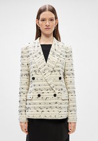 Διπλής όψης σακάκι σε κρεμ και μαύρο υφασμάτινο σχέδιο με οριζόντιες ρίγες, με δύο μπροστινές τσέπες και μαύρα κουμπιά.