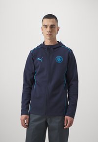 Námornícky zipsový mikina s tyrkysovými akcentmi, zdobená predným logom a kontrastným šitím. Vyrobená z mäkkého materiálu s uvoľneným strihom.