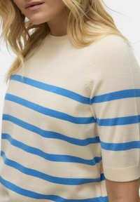 Beige gebreide top met horizontale blauwe strepen, korte mouwen en een ronde halslijn. De stof lijkt zacht en textuur te hebben.