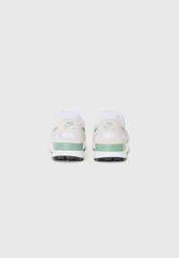 Białe sneakersy z teksturowaną cholewką, miętowymi akcentami i czarną podeszwą. Posiadają wyraźne logo na pięcie i panelach bocznych.