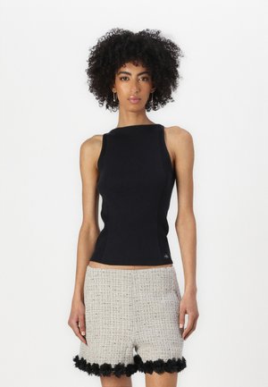 Čierne rebrované tielko s vysokým výstrihom spojené s textúrovanými béžovými šortkami s čiernym kvetinovým lemom na spodku.