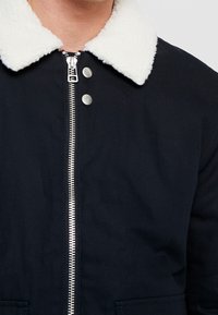 Marinblå jacka med vit fleecekrage, silverfärgad dragkedja och tryckknappar; har en slät textur och en klassisk design med sidofickor.