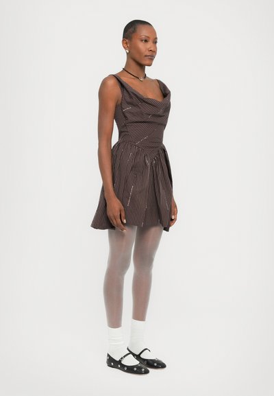 Mouwloze bruin gestreepte jurk met een gedrapeerde halslijn, een aansluitend lijfje en een uitlopende rok. Gecombineerd met grijze maillot en zwarte Mary Jane-schoenen.