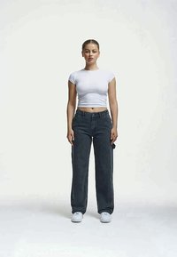 Λευκό κοντομάνικο crop top, συνδυασμένο με σκούρο γκρι φαρδύ παντελόνι. Το μοντέλο φοράει λευκά αθλητικά παπούτσια. Απλός και μοντέρνος σχεδιασμός.