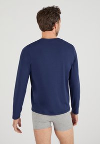 Maglietta a maniche lunghe blu navy realizzata in un tessuto liscio, con scollo rotondo e maniche aderenti, indossata con pantaloni corti grigi.
