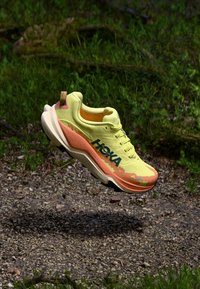 Chaussure de course Hoka présentant un schéma de couleurs jaune vif et orange, un dessus texturé, une semelle rembourrée et un logo bien en vue sur le côté.