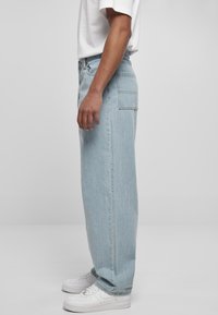 Light blue denim jeans with a straight fit, featuring a back pocket and a zip fly. Paired with white sneakers and a white t-shirt.