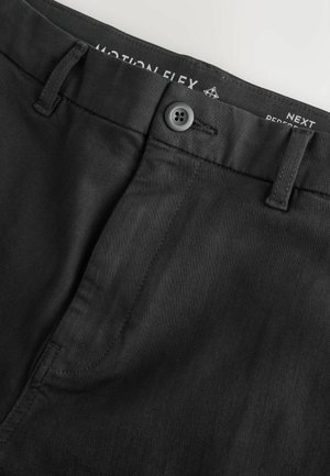 Pantaloni neri con una texture liscia, dotati di chiusura con bottone, passanti per cintura e sottili dettagli in cucitura. Etichetta del marchio visibile all'interno.