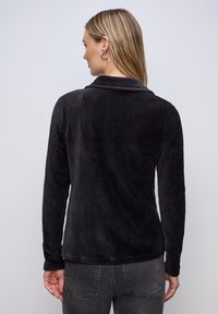 Chemise en velours côtelé noire à manches longues, col à revers et lignes verticales texturées. Finition en tissu lisse, coupe décontractée avec coutures visibles.