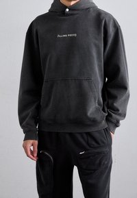 Sudadera de color gris oscuro hecha de una tela suave, con un bolsillo frontal, puños acanalados y un pequeño logo blanco de "FILLING PIECES" en el pecho.