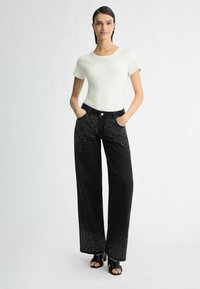 Wit kortemouwen top met een ronde hals, gecombineerd met zwarte wijde jeans met verspreide rhinestones en voorzakken. Zwarte sandalen.