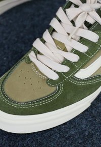 Grønne og beige semskede sneakers med hvite snører og søm. Har en rund tå og stripe-detalj på siden. Gummisåle.
