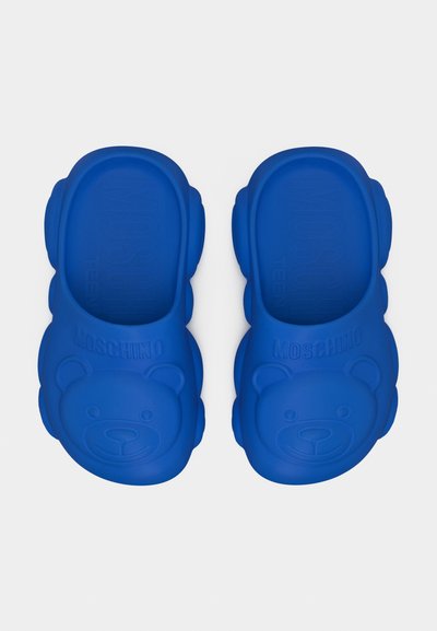 Μπλε σανδάλια με λάστιχο, με ανάγλυφα πρόσωπα αρκουδάκια και λογότυπο "Moschino" στα λουριά, κατασκευασμένα από μαλακό καουτσούκ.