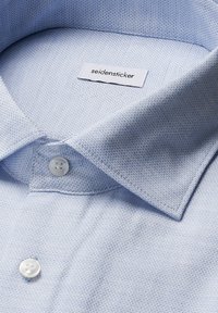 Camicia colletto azzurro in tessuto strutturato, con etichetta bianca, chiusura a due bottoni e un design classico.