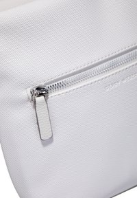 Pañuelo texturizado blanco con cierre con cremallera, herrajes de cremallera plateados y una pequeña pestaña de cuero blanco. Presenta el nombre de la marca en relieve.