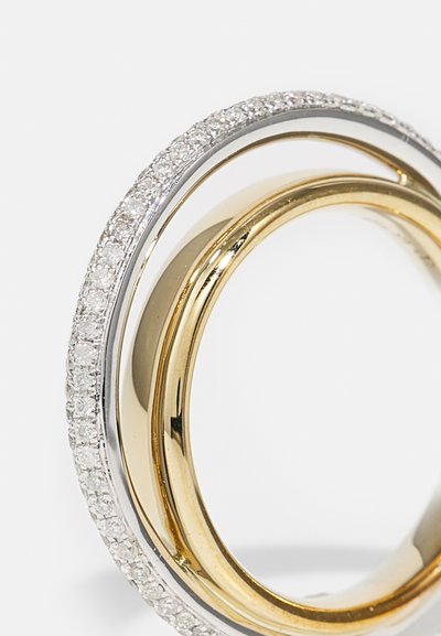 Anello in oro e argento con un design intrecciato. Un motivo è in oro liscio, mentre l'altro presenta piccole gemme trasparenti lungo il bordo.