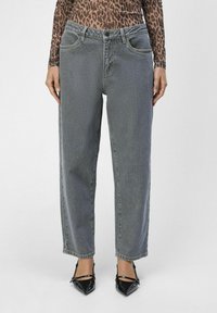 Jeans de mezclilla gris con corte recto, cinco bolsillos y un ligero desgastado. Combinados con tacones de charol negros y punta afilada.